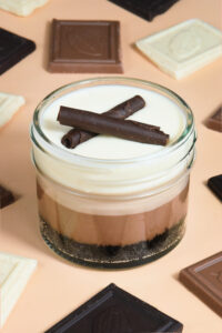 alt="Triple chocolate cheesecake jar with Oreo crust, layers of dark, milk, and white chocolate cheesecake, topped with milk chocolate ganache and a chocolate cigarette — made from scratch in San Antonio, Texas"