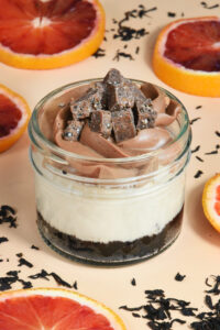 alt="A rich Earl Grey Cheesecake in an Oreo cookie crust, layered with bright Orange Pastry Cream, tangy Blood Orange Confit, smooth Chocolate Earl Grey Ganache, and finished with a crisp Sesame Chocolate Crunch — handmade in San Antonio, Texas"