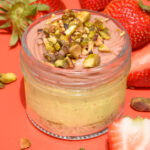 alt="Pistachio Mousse Cheesecake jar with Graham Crust, layered with Strawberry Confit, and topped with Strawberry Ganache and Pistachio Pieces — made from scratch in San Antonio, Texas"