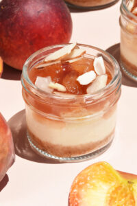 alt="Silky Vanilla Cheesecake layered with Baked Almond Cream. Finished with Peach Jam made from fresh peaches and a sprinkle of Toasted Almond Petals. Perfect fruity and fresh summer flavor. Made from scratch in San Antonio Texas"