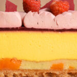 alt="Light Mango Cheesecake layered with Almond Frangipane and sweet Dried Mango Pieces. Topped with tart Raspberry Compote, silky Raspberry Ganache, Fresh Raspberries, and a crisp Raspberry Chocolate Crunch, made from scratch in San Antonio, Texas"
