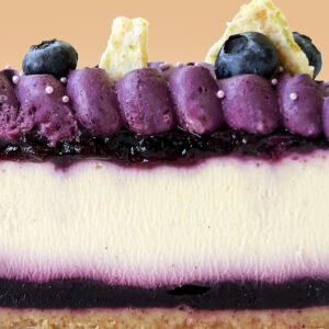 alt="Blueberry cheesecake with graham crust, blueberry jam, vanilla cheesecake filling, blueberry ganache, and white chocolate lime zest crunch made in San Antonio, Texas"