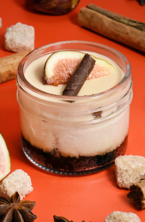 alt="Layered cheesecake jar made from scratch in San Antonio — starting with an Oreo crust, chai cheesecake, butterscotch crunch, silky butterscotch mousse, topped with fresh fig and a dark chocolate cigarette."