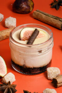 alt="Layered cheesecake jar made from scratch in San Antonio — starting with an Oreo crust, chai cheesecake, butterscotch crunch, silky butterscotch mousse, topped with fresh fig and a dark chocolate cigarette."