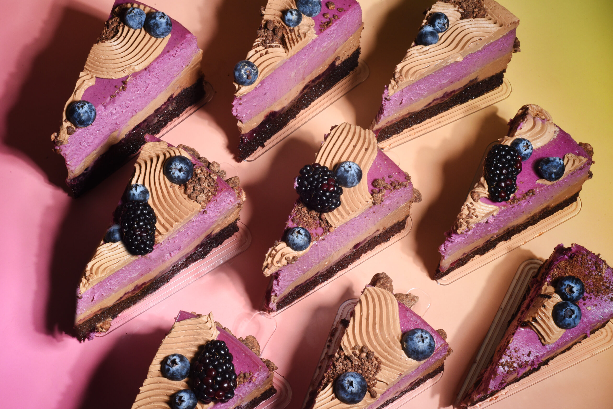 A multi-layered dessert featuring chocolate cake soaked in berry syrup, topped with berry cheesecake, milk chocolate ganache, and mezcal-infused wild berry jam. The dessert is finished with a dusting of chocolate soil and fresh seasonal berries.